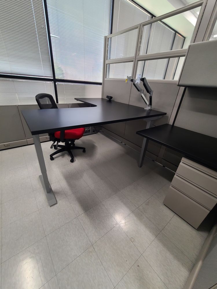 Black office desk with red chair, grey cubicle walls, and large windows.