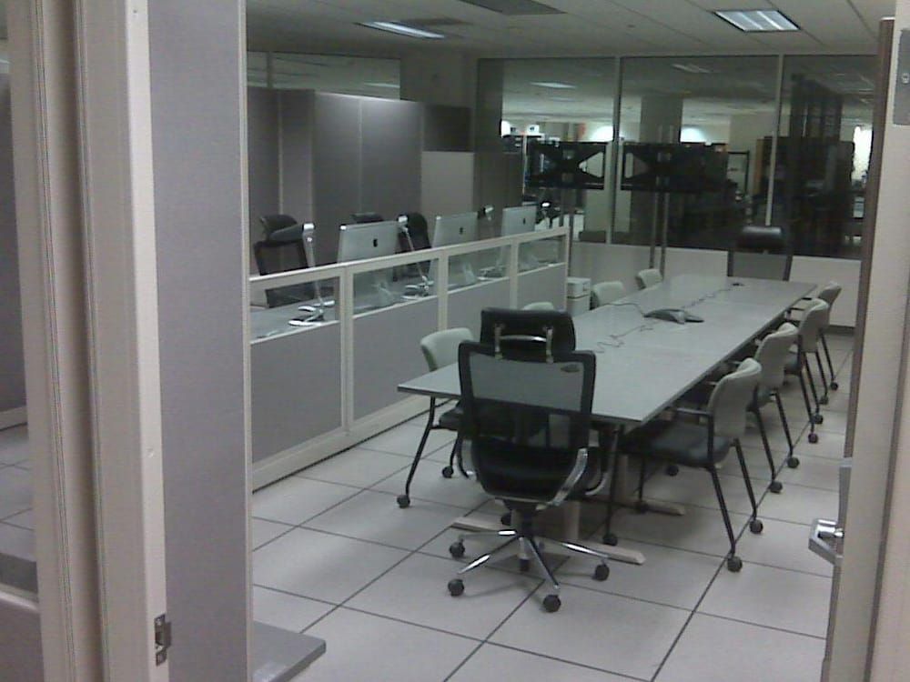 Conference room with a long table, chairs, and cubicles visible through a doorway.
