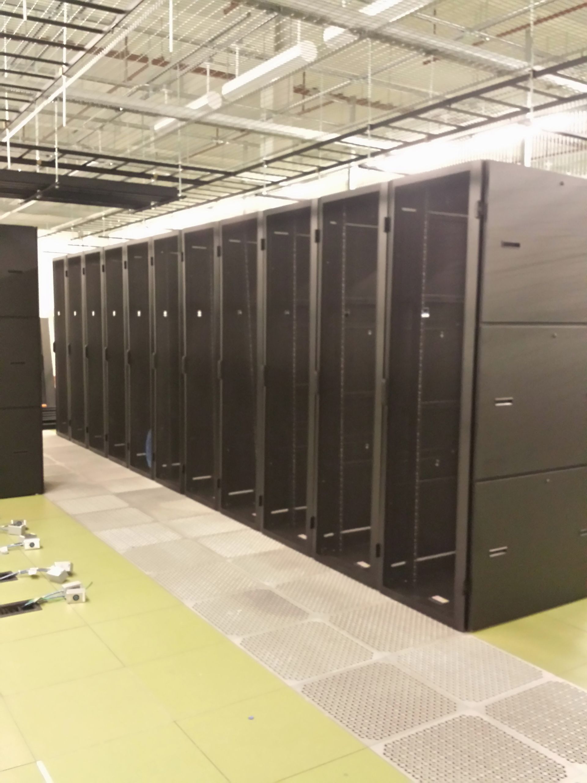 Row of empty black server racks in a warehouse with a metal floor.