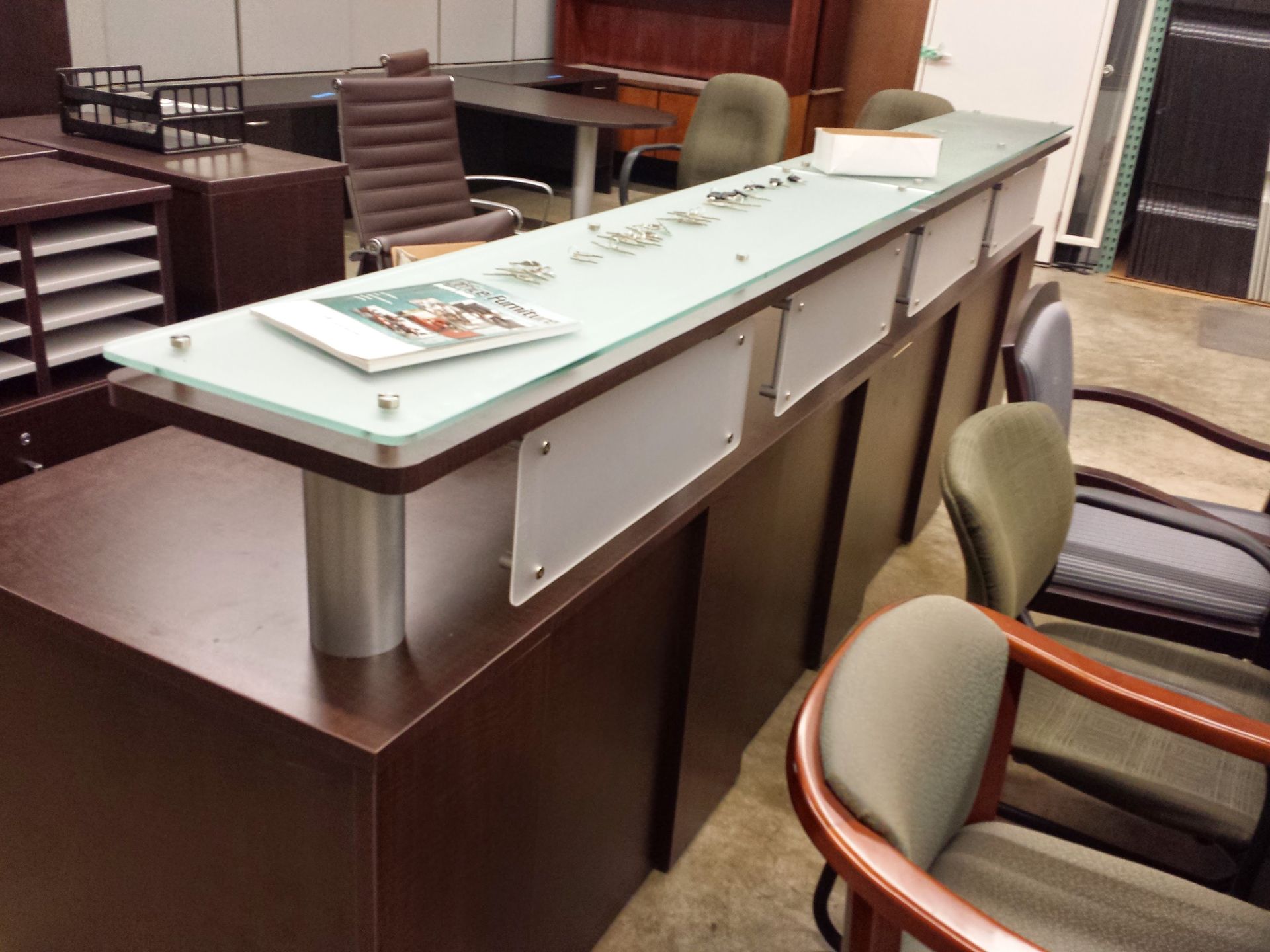 Dark brown reception desk with glass top, small objects, and chairs.