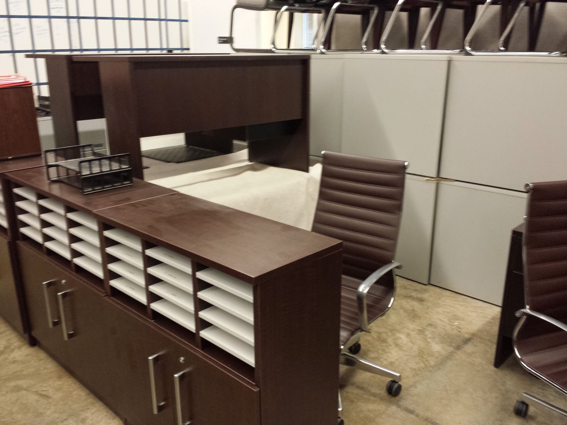 Office furniture display: desk, filing cabinet with mail slots, and brown leather chairs.