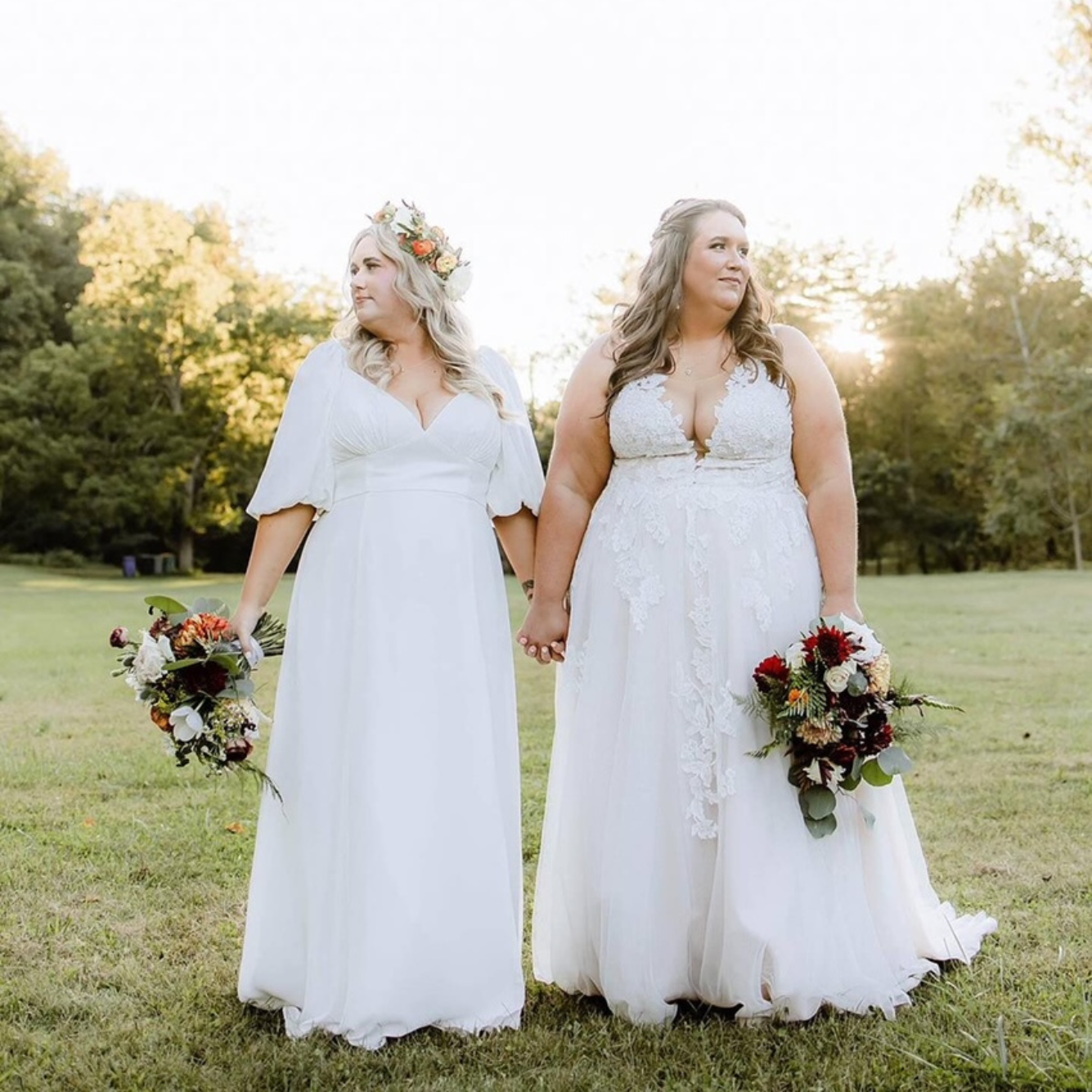 Two plus size brides are holding hands in a field.