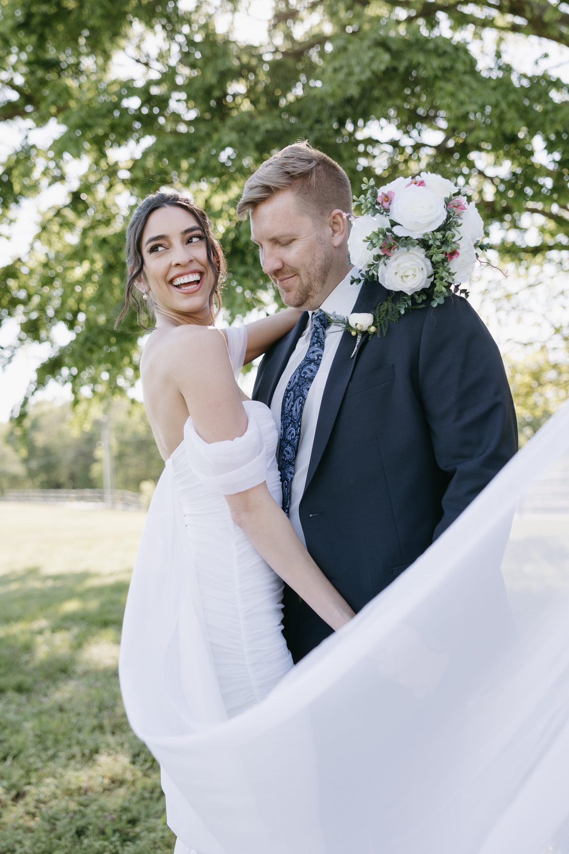 A bride and groom are posing for a picture with their veil blowing in the wind.