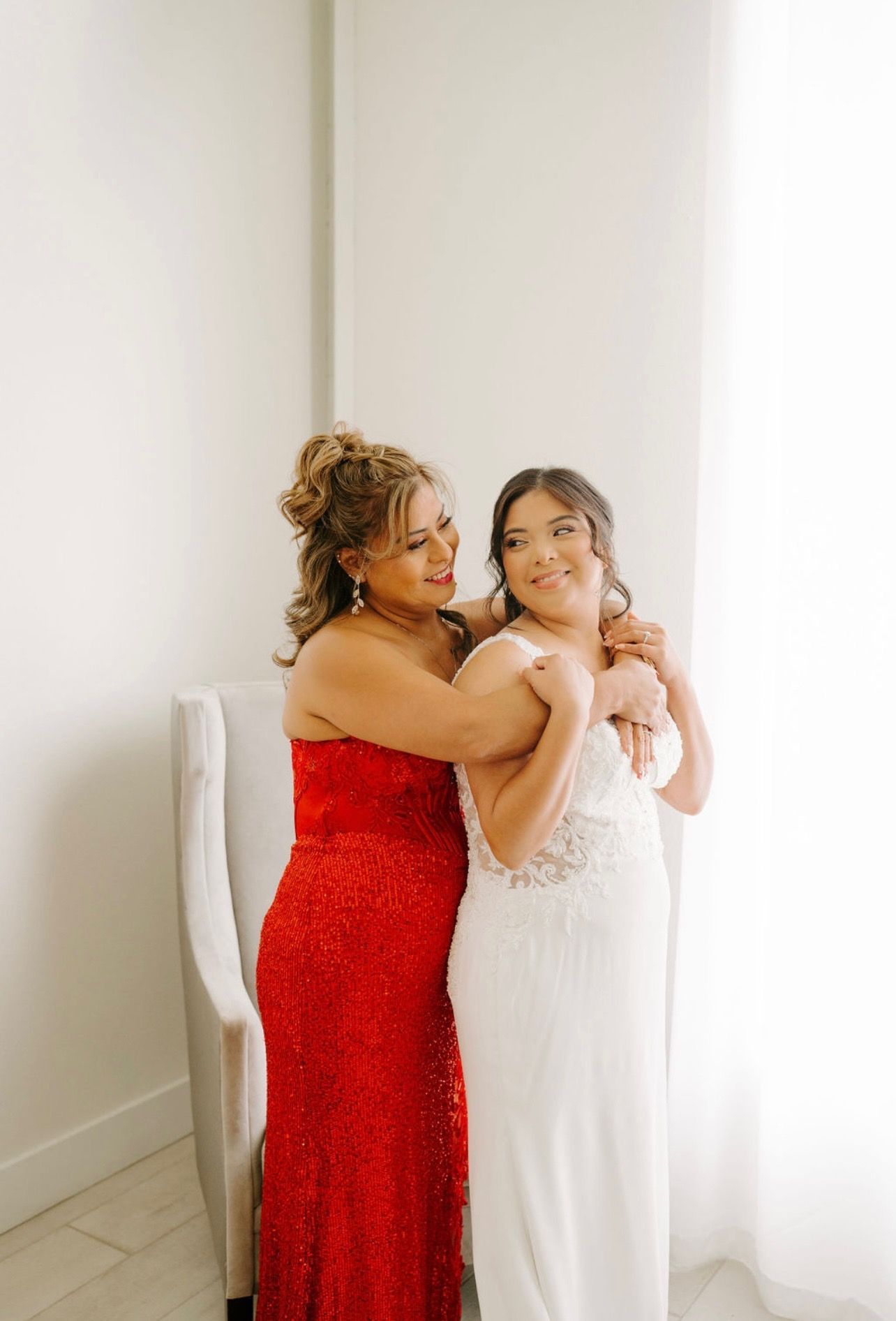 A woman in a red dress is hugging a woman in a white dress.