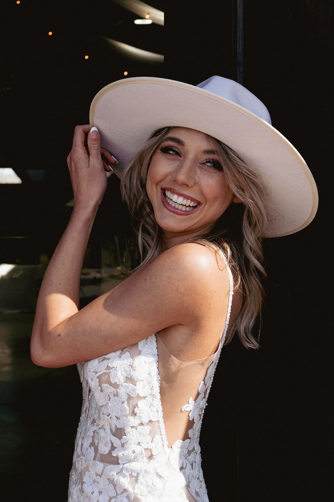 A woman in a wedding dress and hat is smiling.