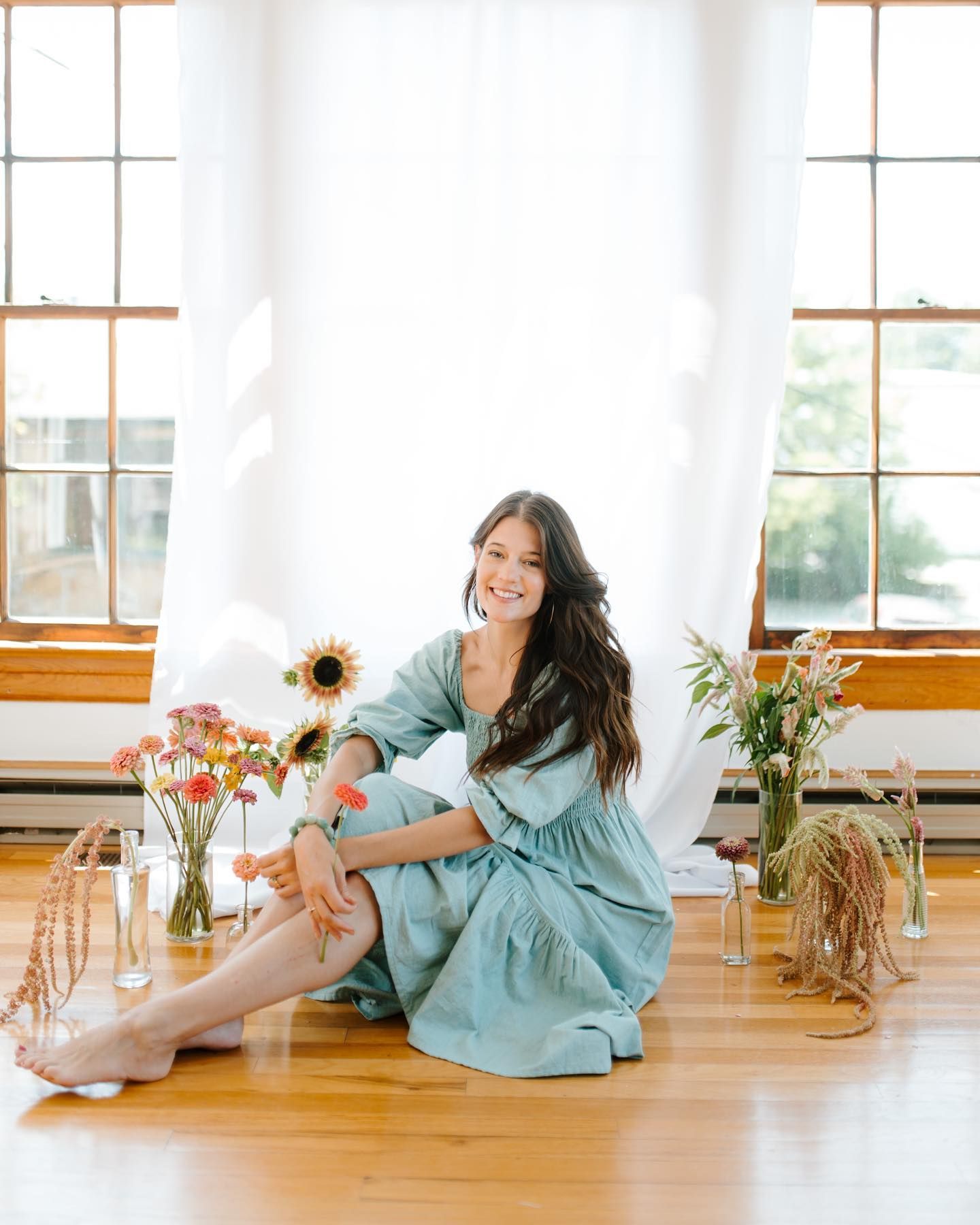 A woman in a blue dress is sitting on the floor in front of a window.