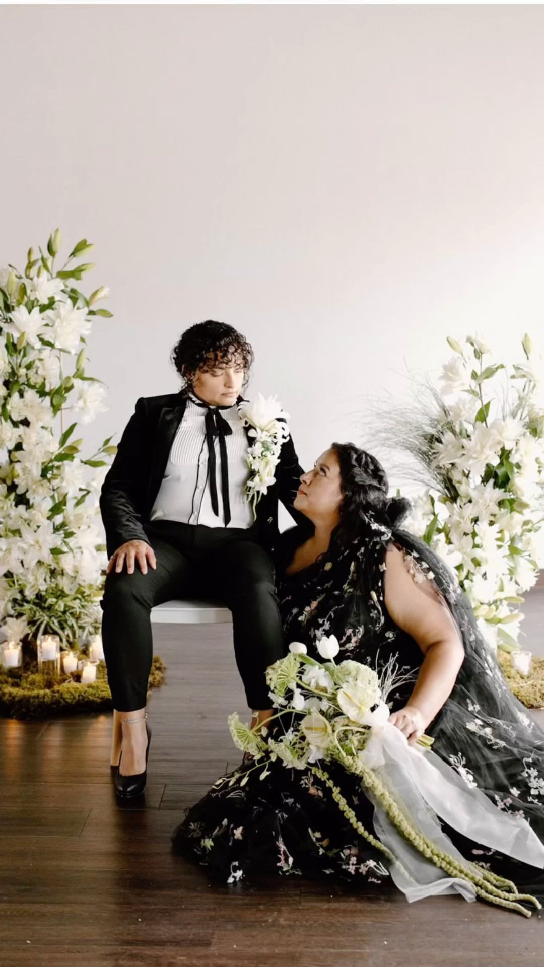 A woman in a black dress is sitting next to a woman in a tuxedo.