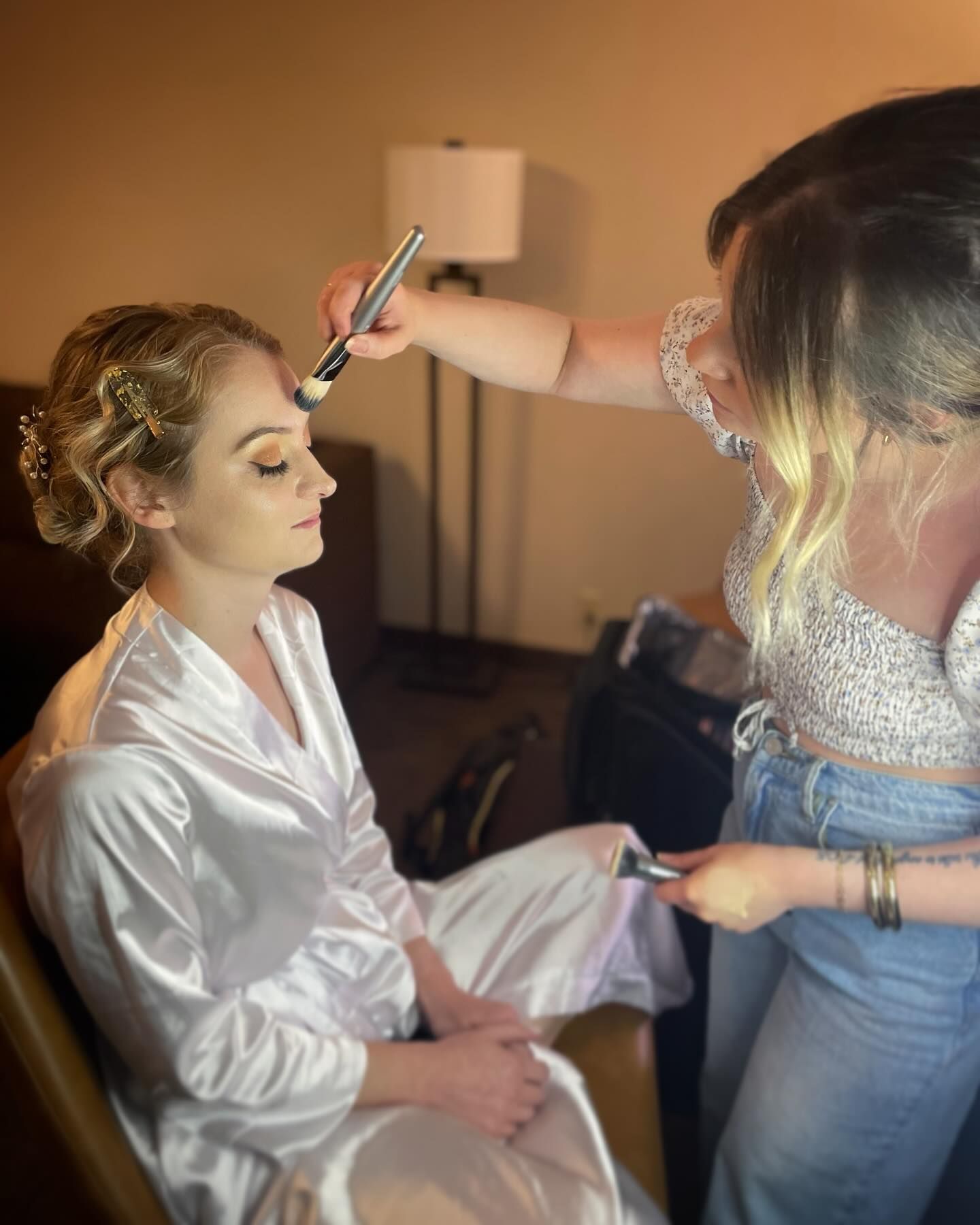 A woman is getting her makeup done by a makeup artist in a room.
