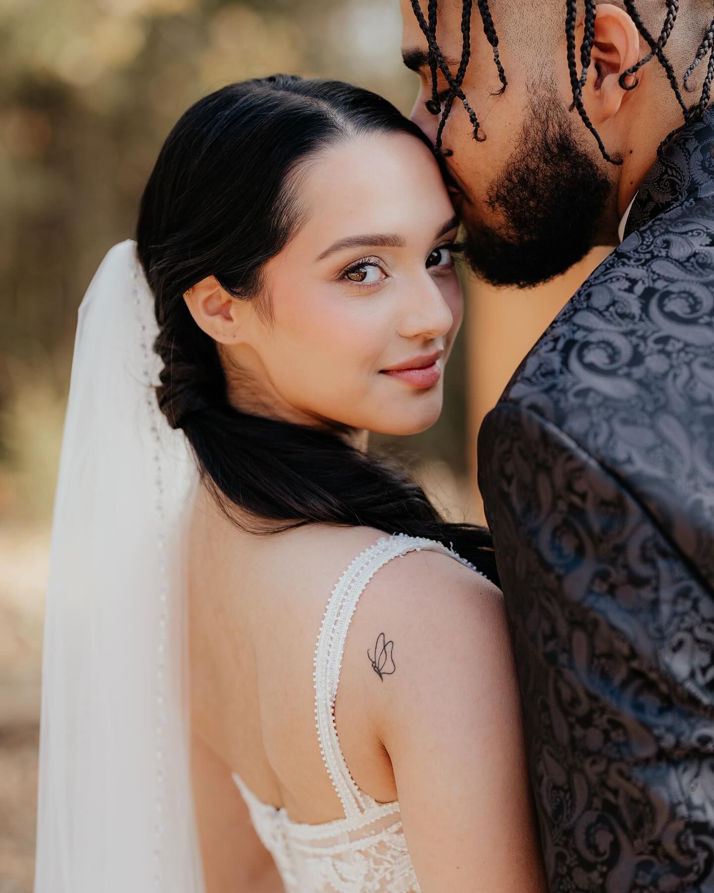 A bride and groom are posing for a picture and the bride has a tattoo on her arm.