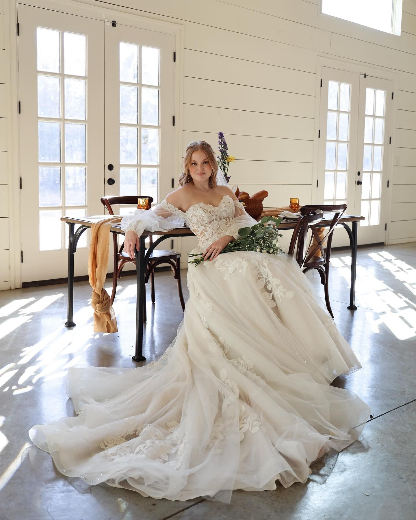 A woman in a wedding dress is sitting at a table with a bouquet of flowers.