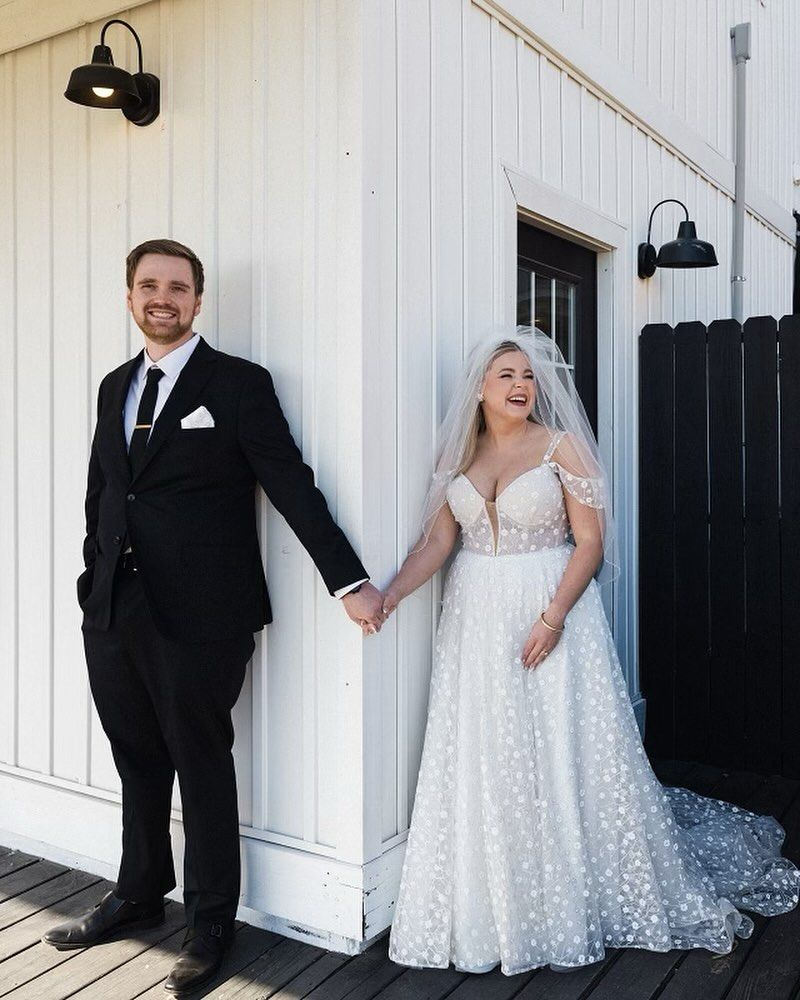 A bride and groom are standing next to each other holding hands in front of a white building.