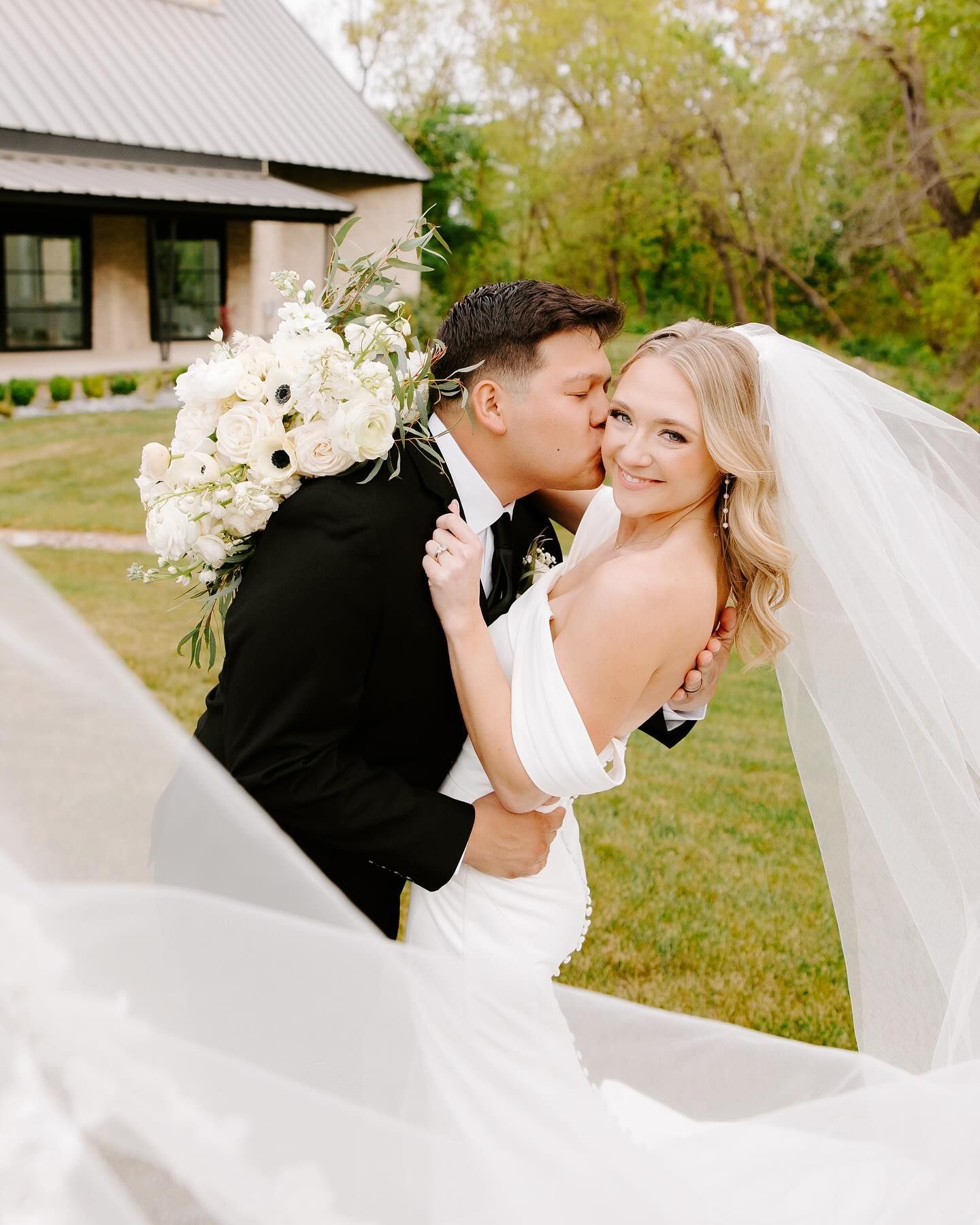 A bride and groom are kissing in front of a house.