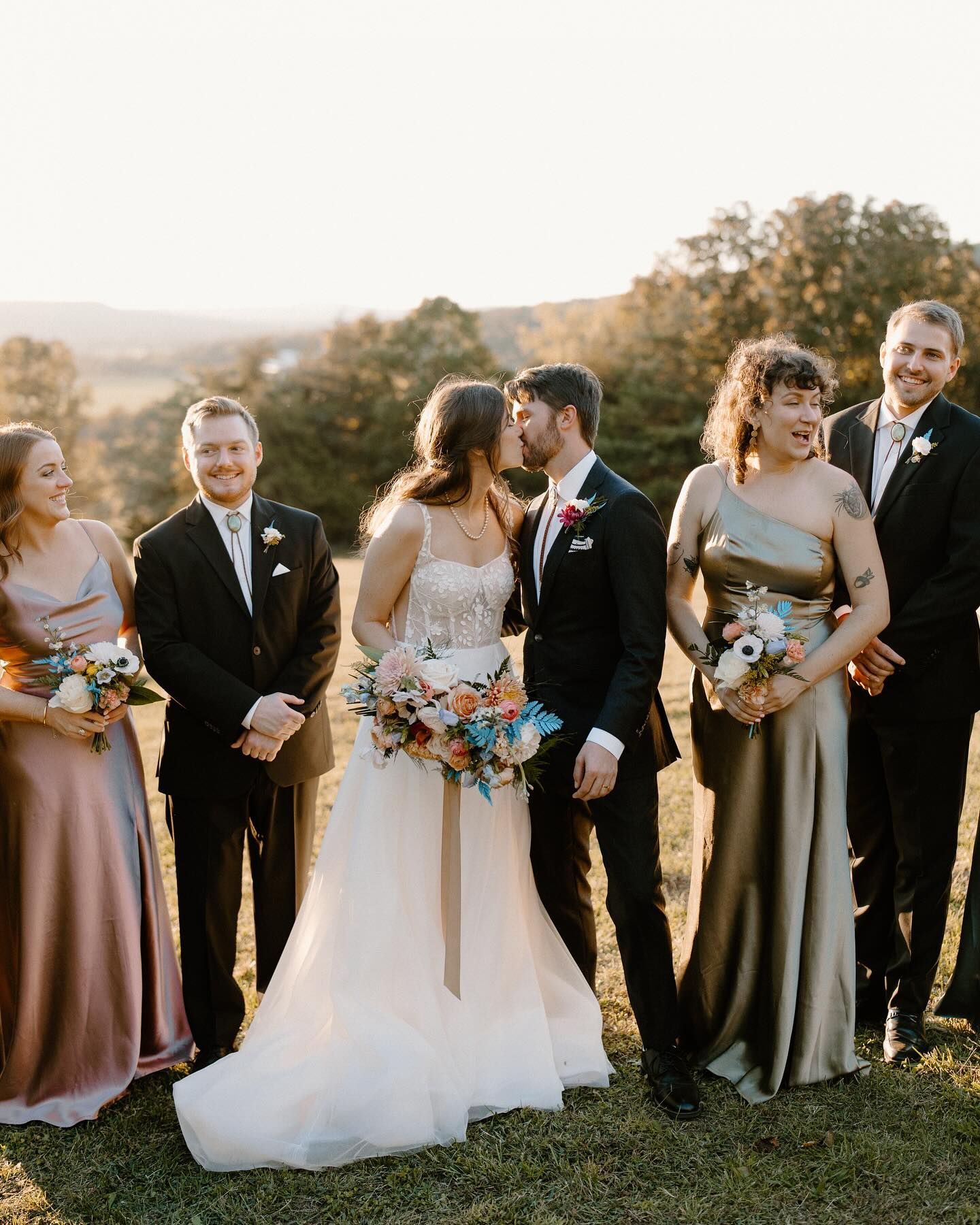 A bride and groom are kissing in front of their wedding party.