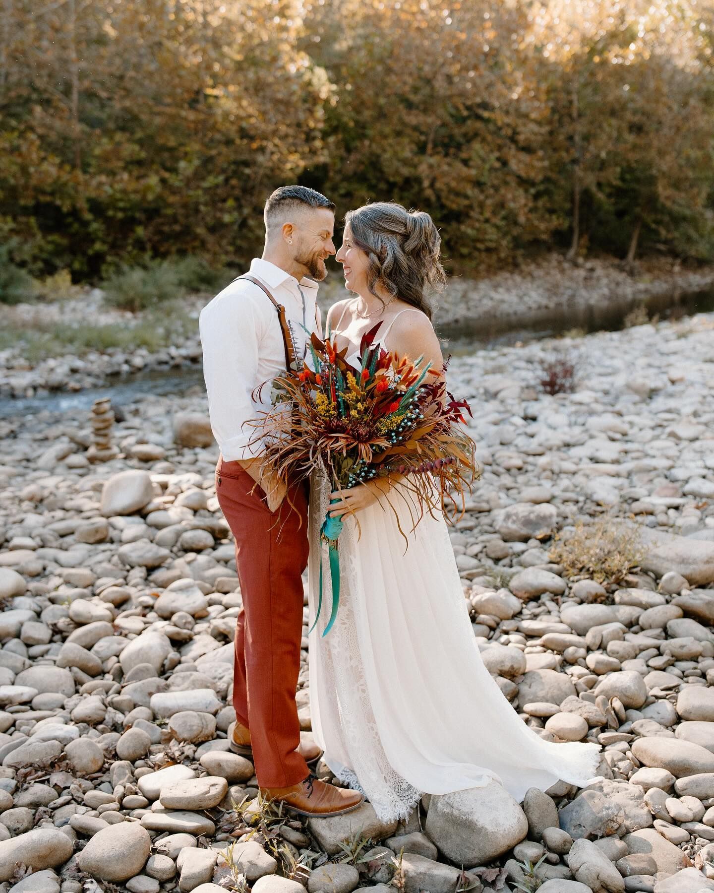 A bride and groom are standing next to each other on a rocky beach.