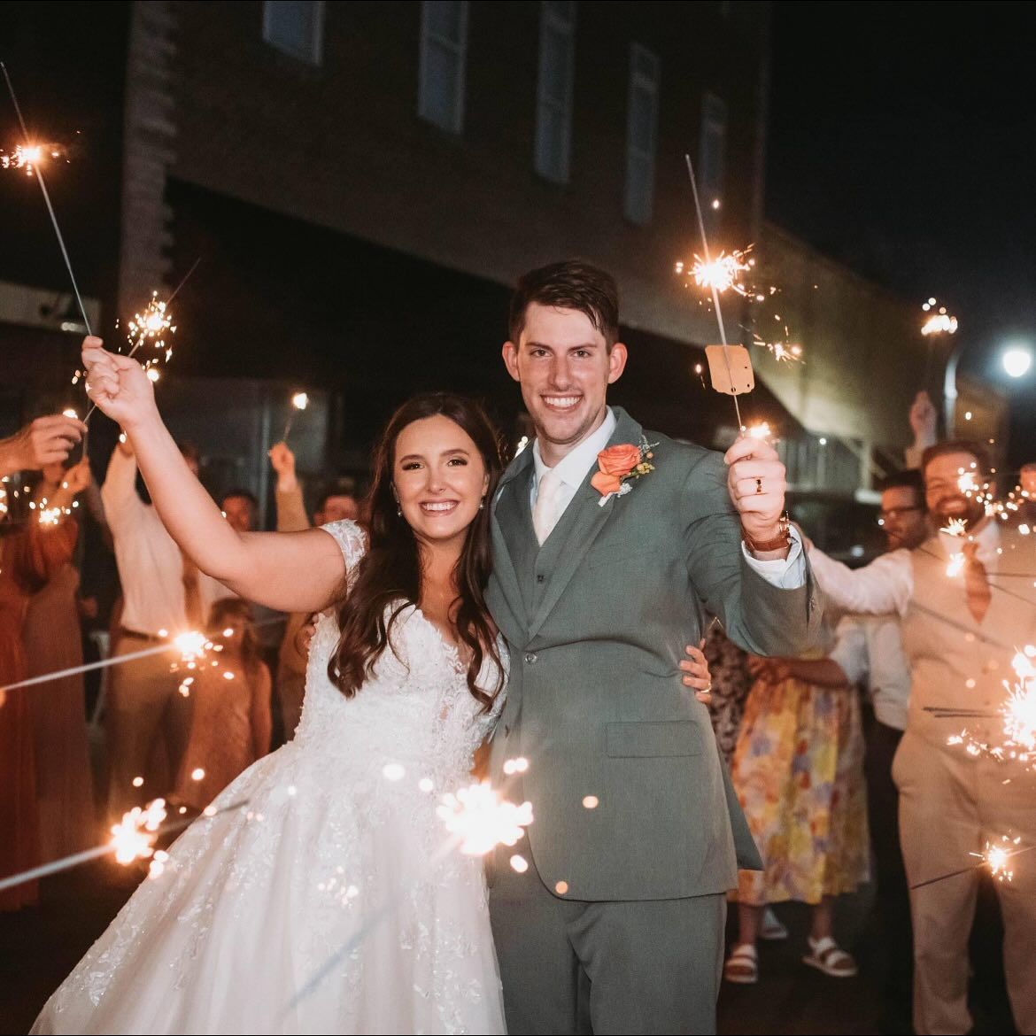 A bride and groom are posing for a picture while holding sparklers.