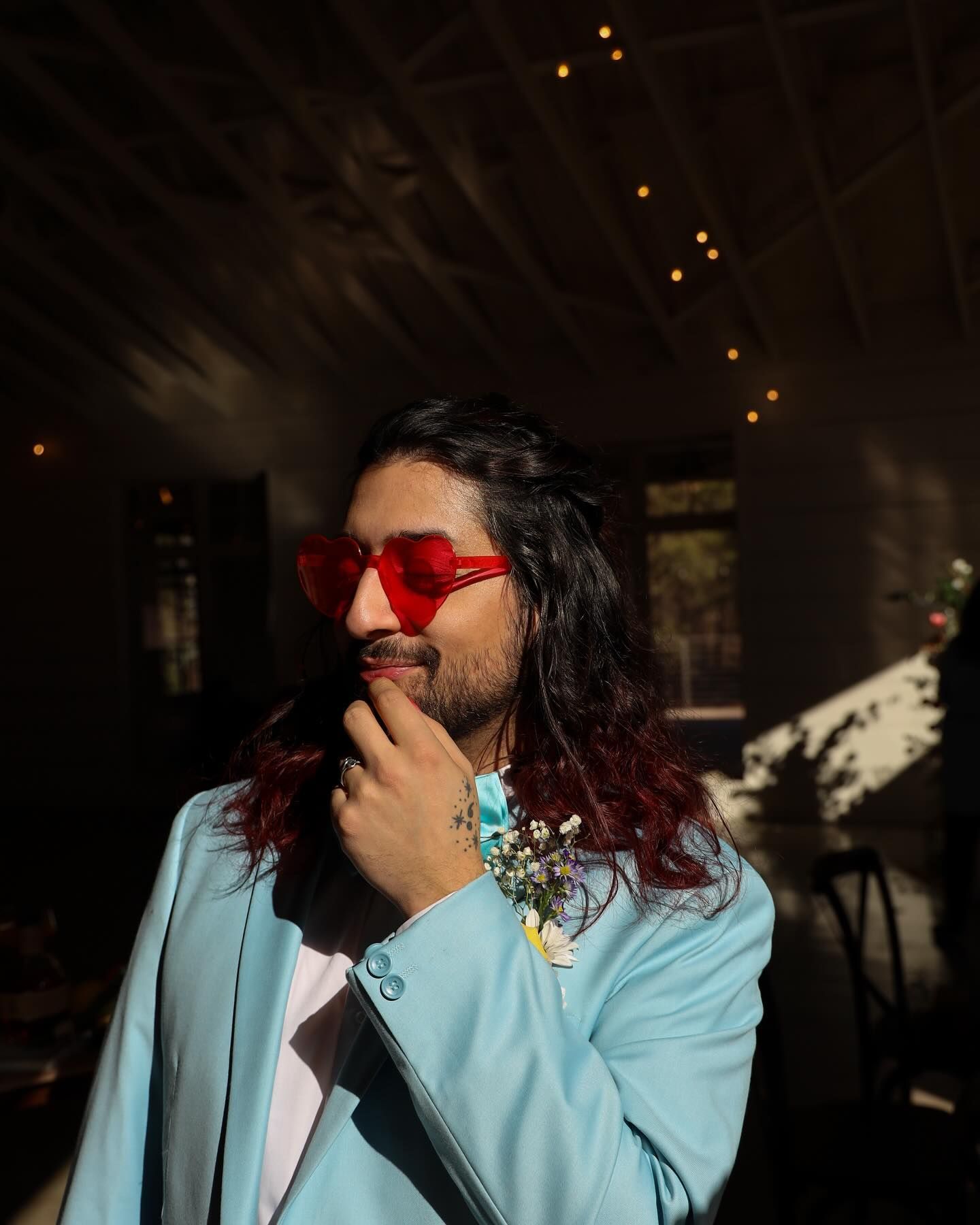 A man wearing a blue jacket and red sunglasses is standing in a dark room.