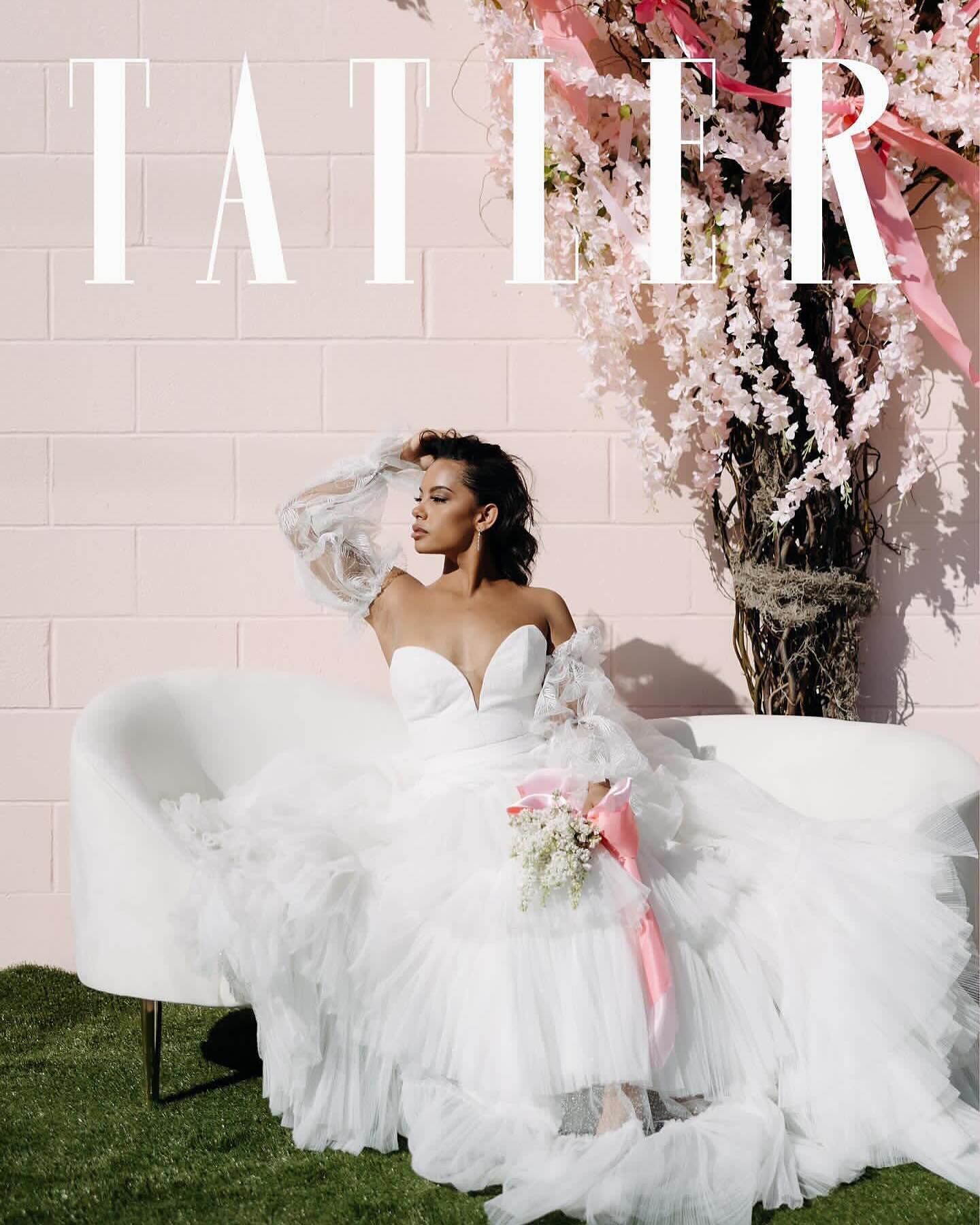 A woman in a wedding dress is sitting on a couch in front of a pink wall.