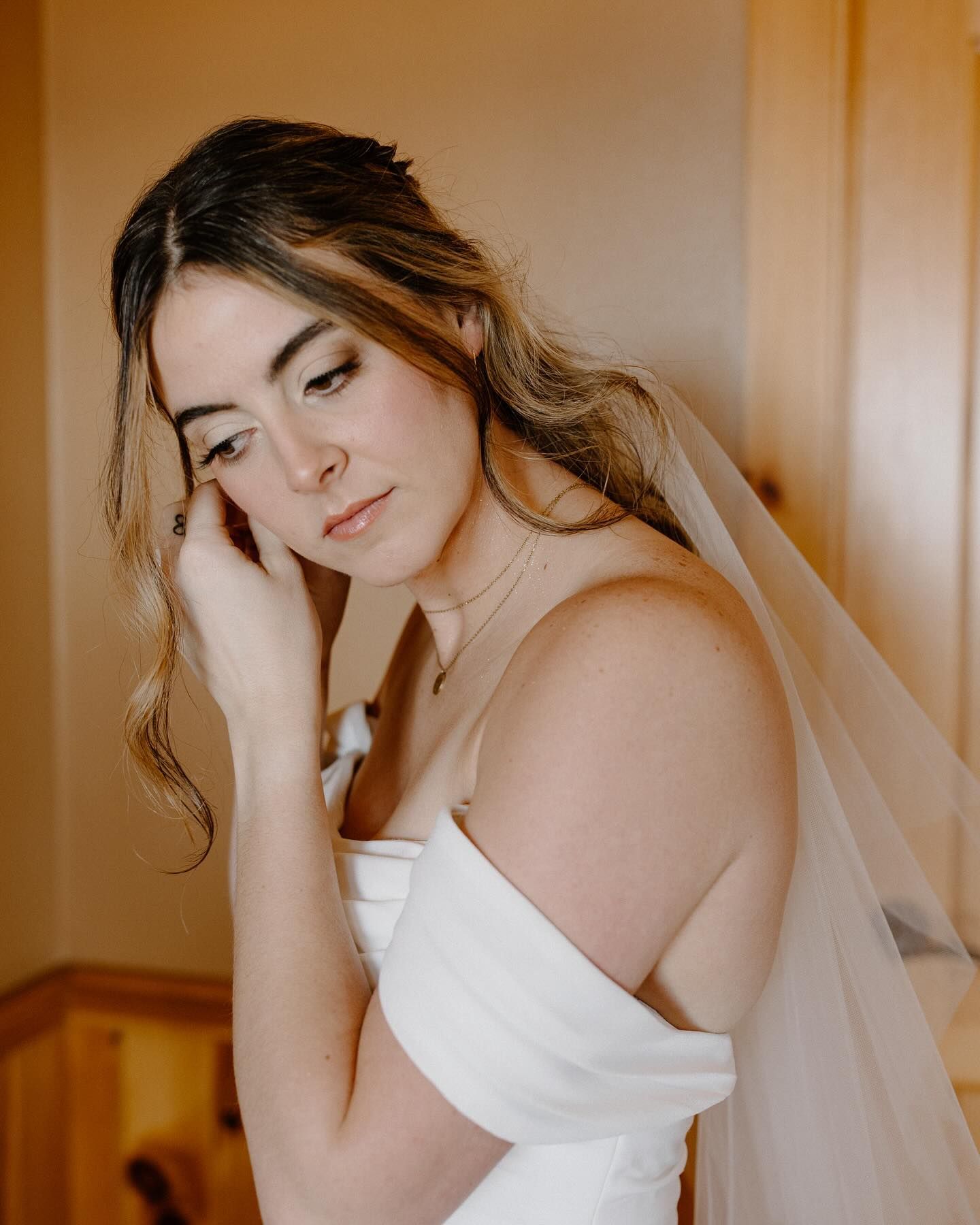 A woman in a wedding dress and veil is touching her ear.