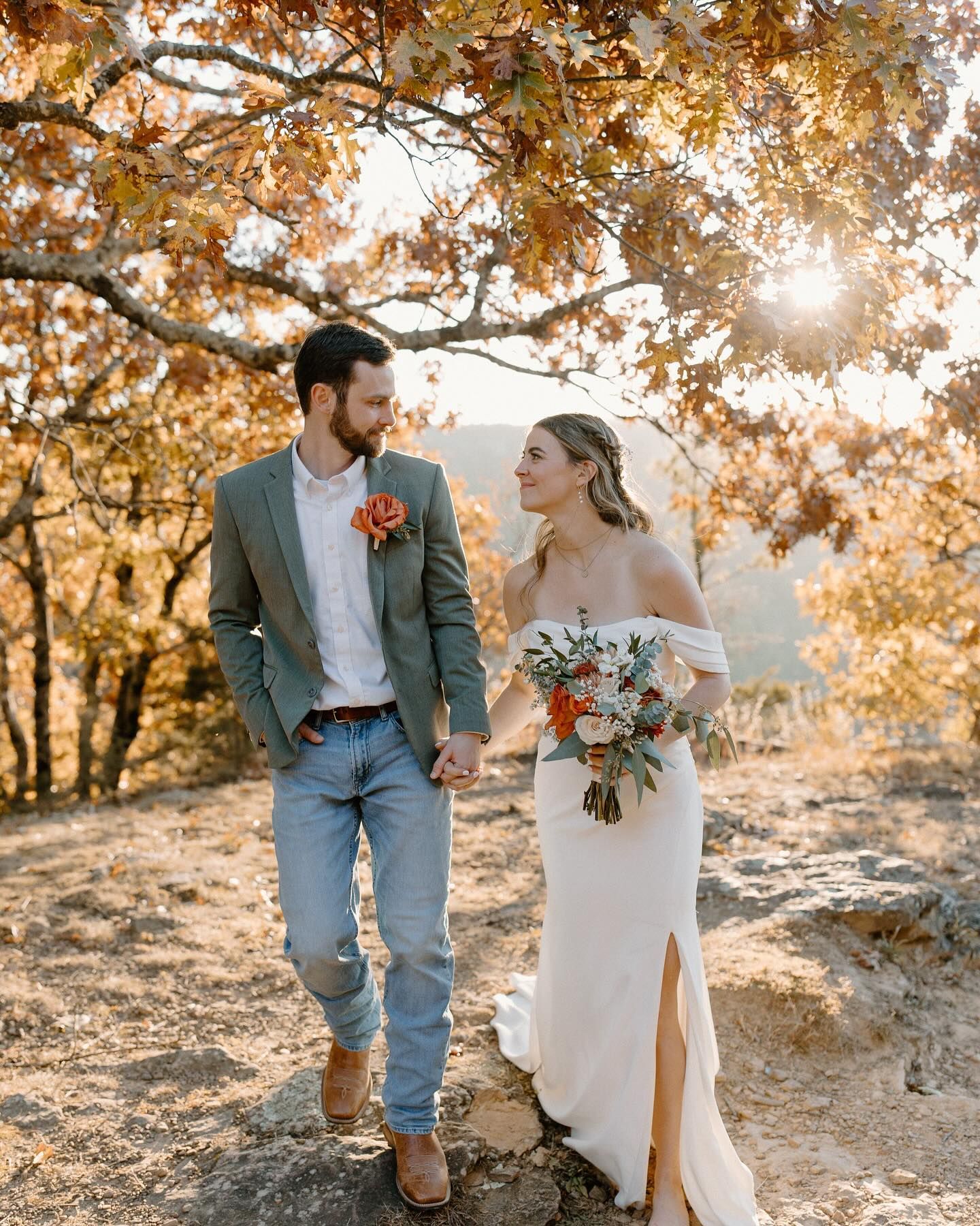A bride and groom are holding hands and walking in the woods.