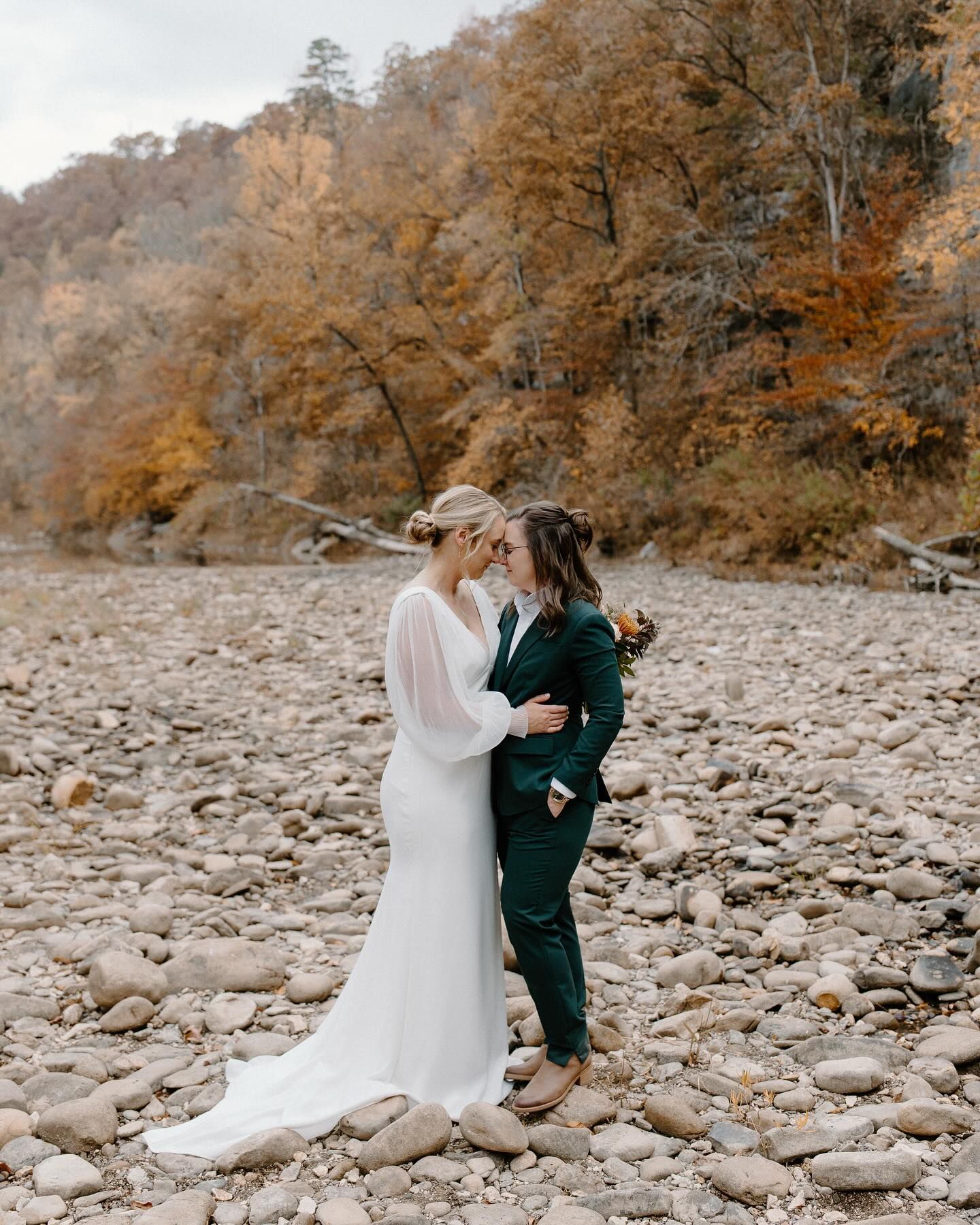A bride and groom are standing next to each other on a rocky beach.