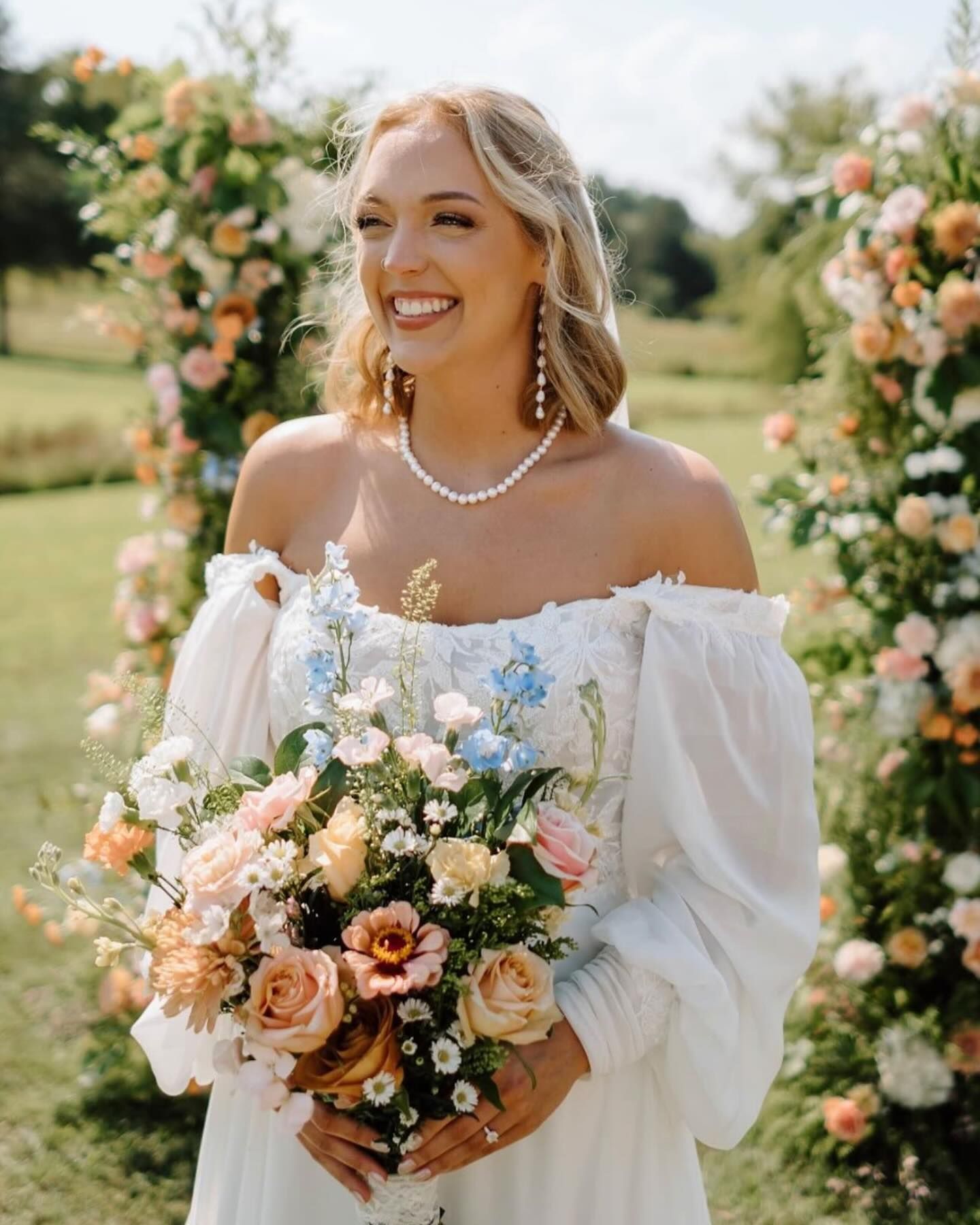 A bride in a white dress is holding a bouquet of flowers and smiling.