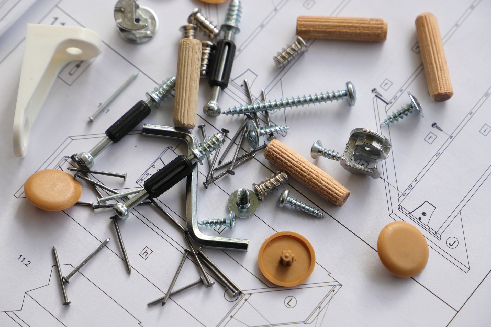 Hardware fasteners scattered on a furniture assembly plan. Includes screws, dowels, and brackets.