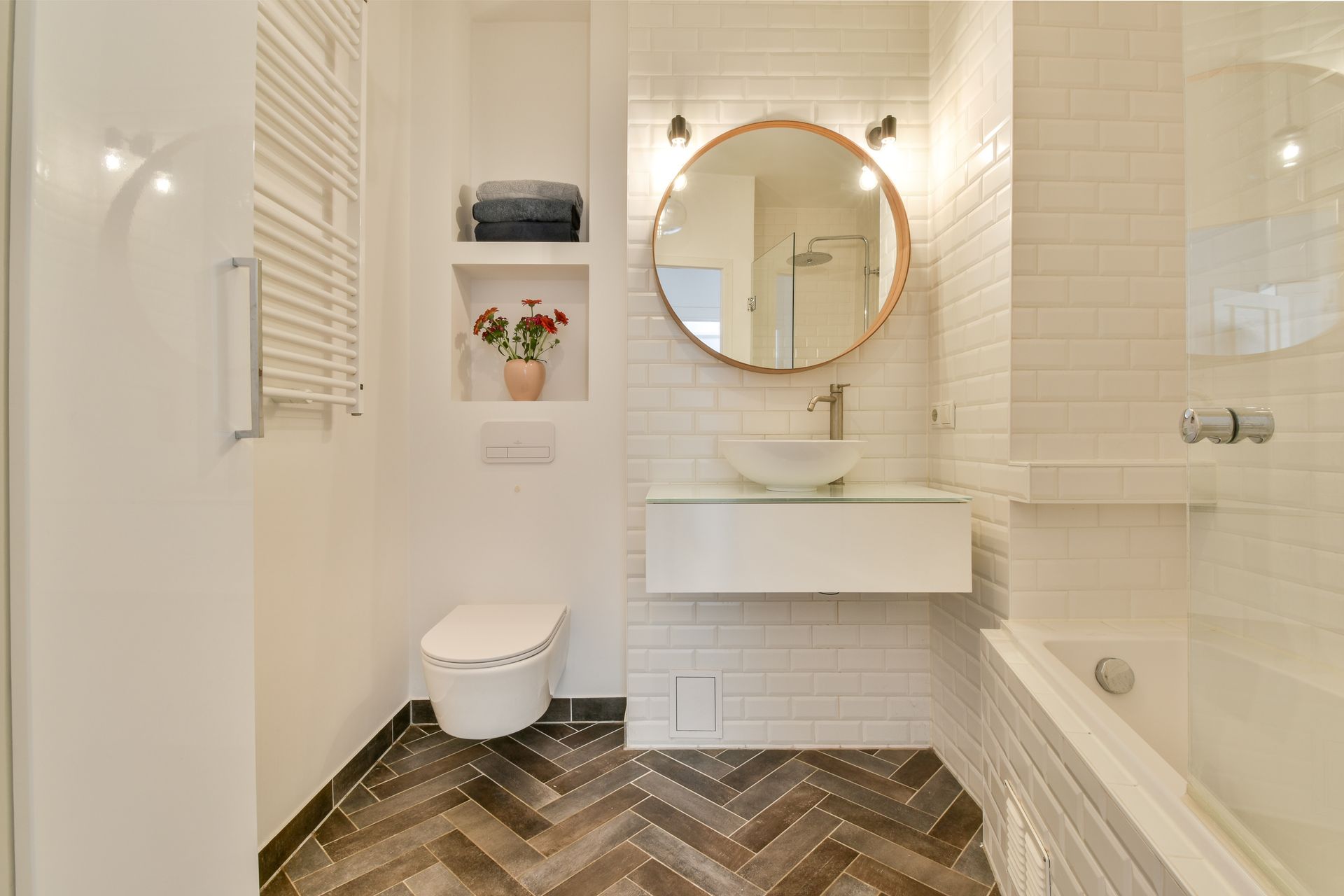 Modern white bathroom with subway tile walls, wood-pattern floor, and a round mirror above a white sink.