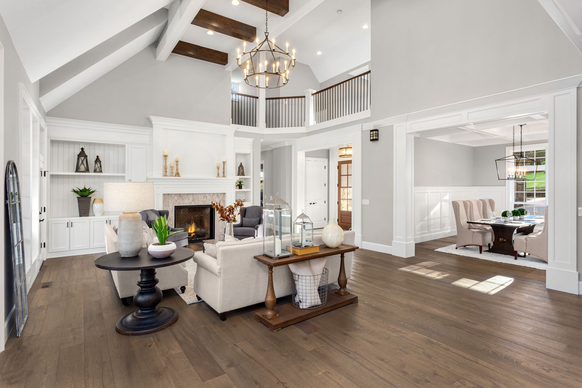 Spacious living room with vaulted ceiling, fireplace, and dining room visible. Wooden floors and neutral color scheme.