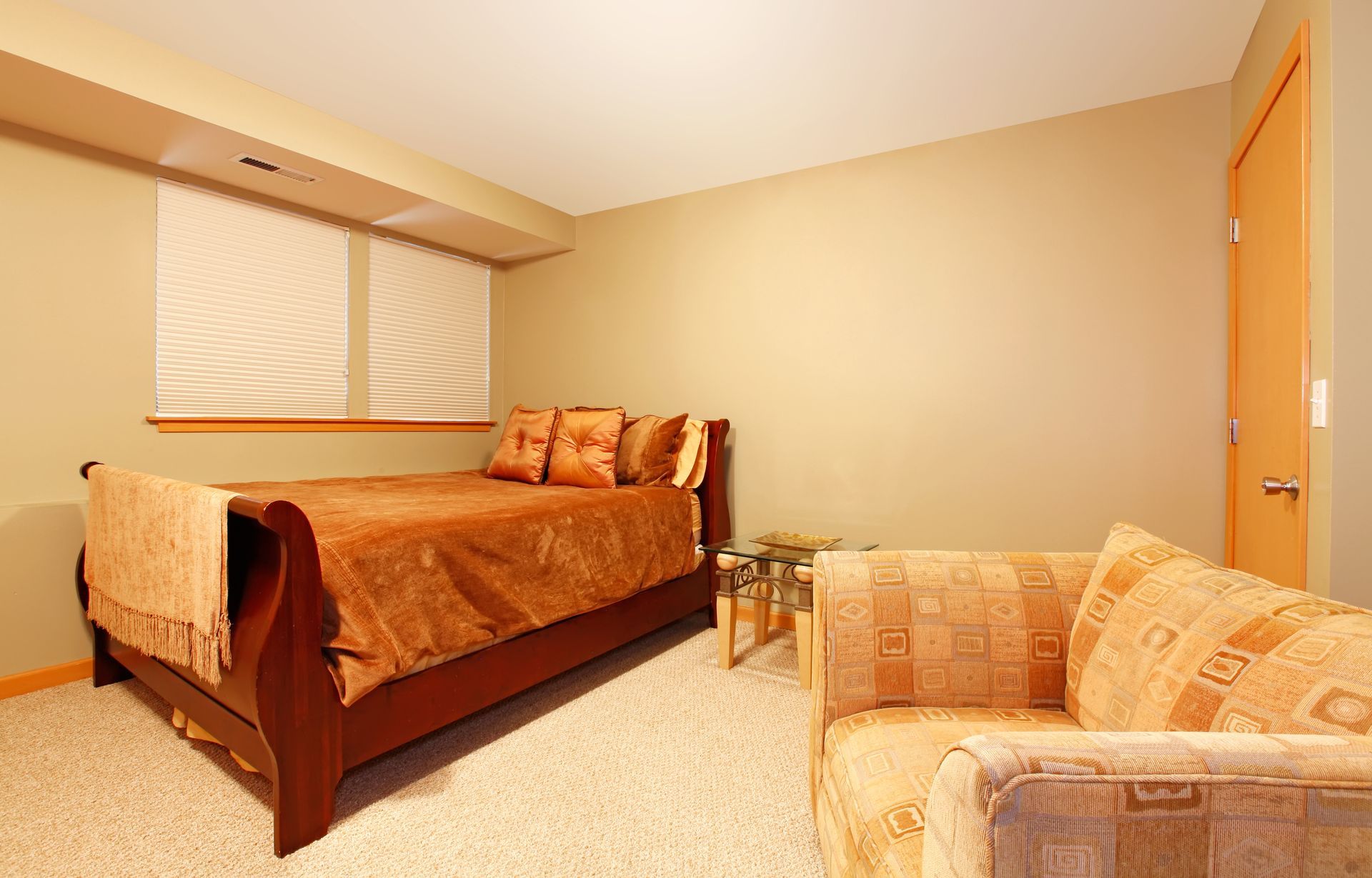 Bedroom with a brown bed, beige carpet, and a matching loveseat. A window with blinds and a closed door are also visible.