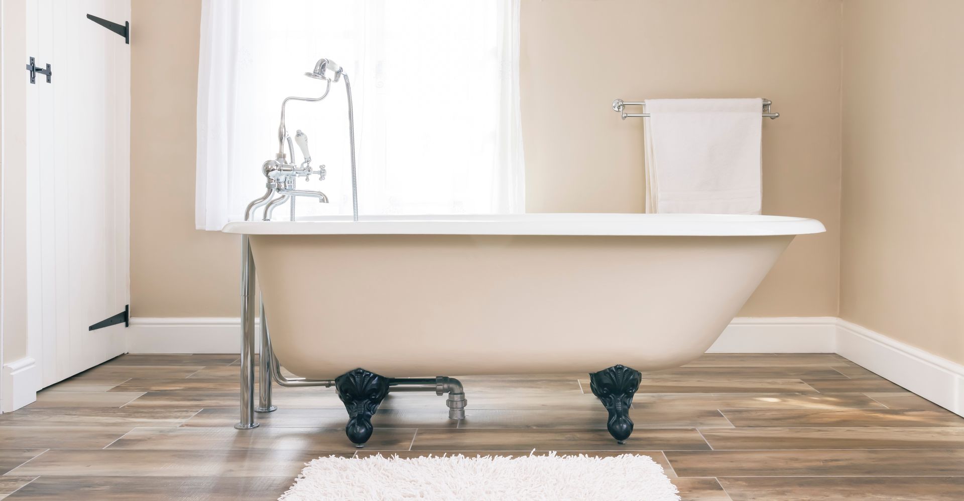 Claw-foot bathtub in a neutral-toned bathroom with a window and towel rack.