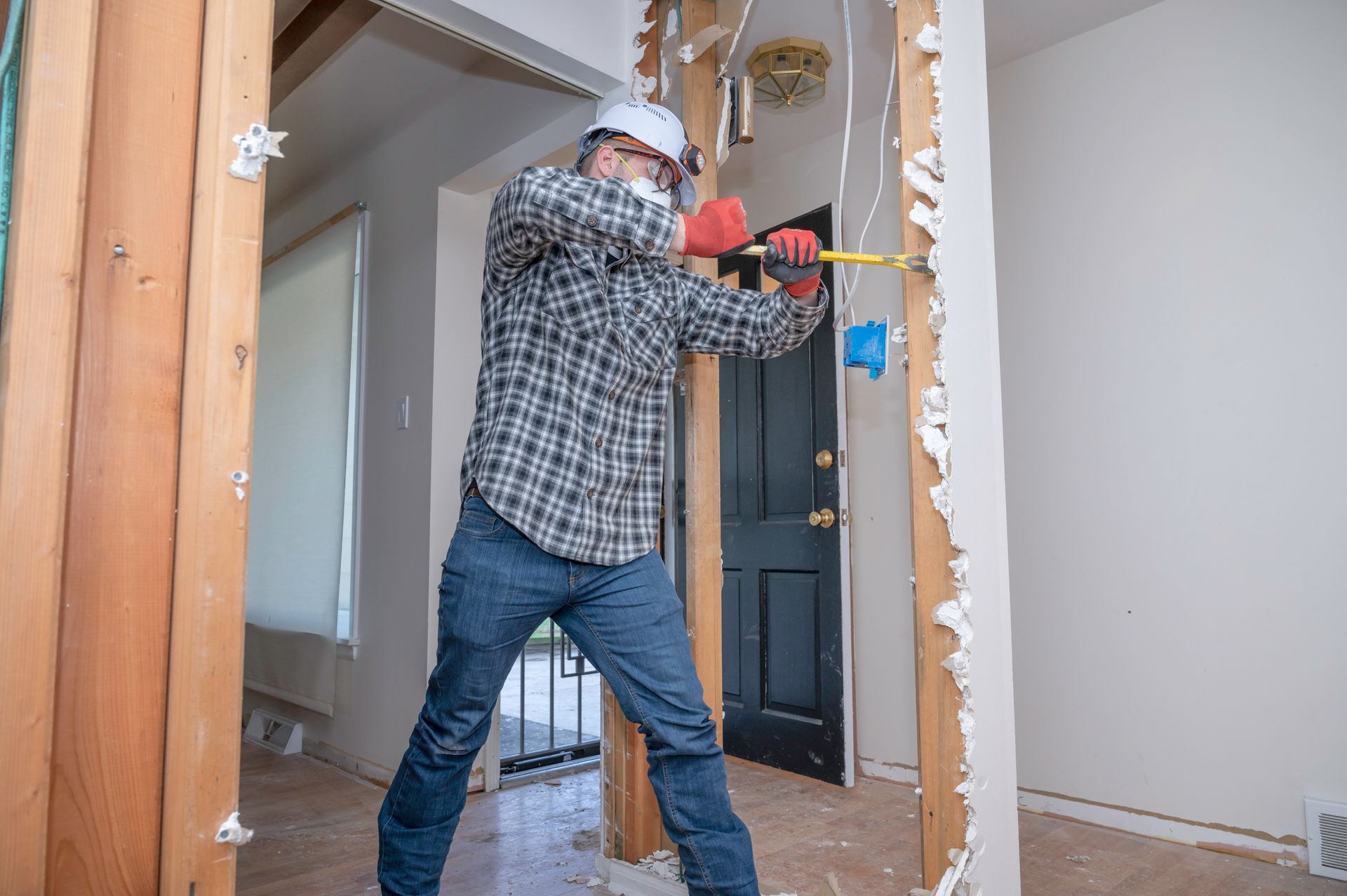Person in hard hat and mask demolishing wall with a hammer. Interior shot.