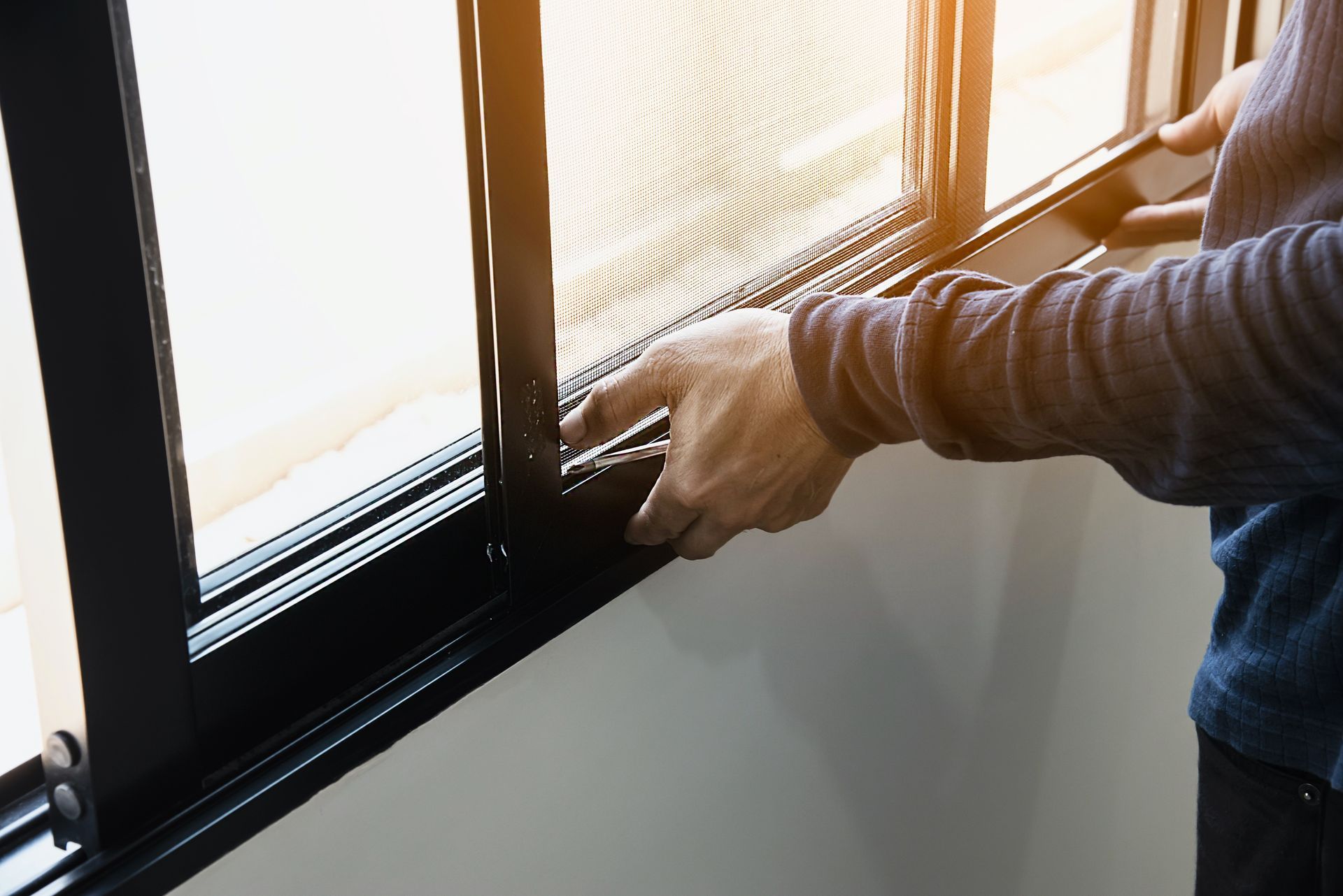 Person installing a black window screen in a white-walled room.