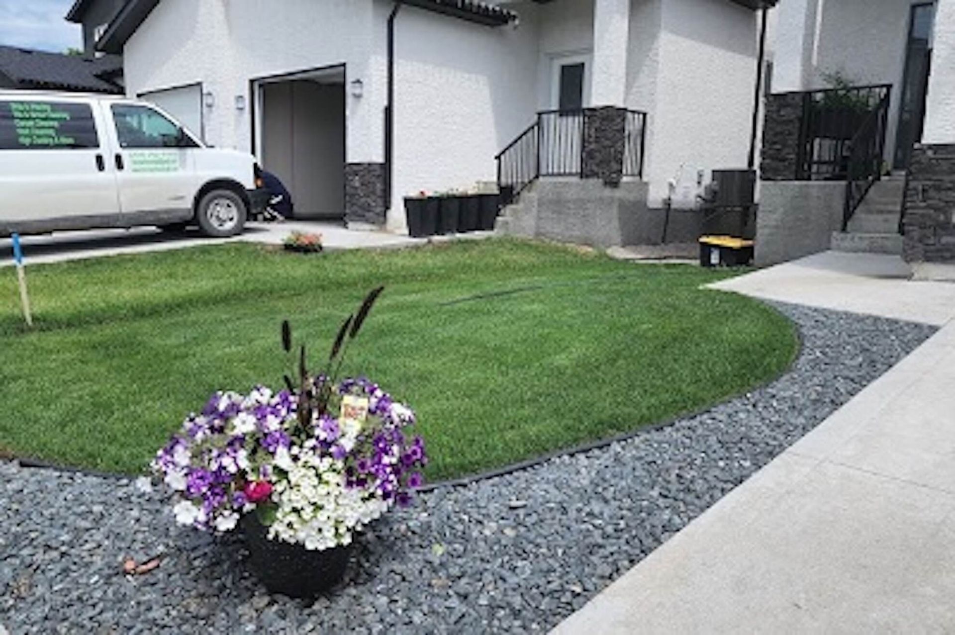 A potted flower arrangement sits on a gray rock garden bed next to a freshly laid lawn and a white work van.