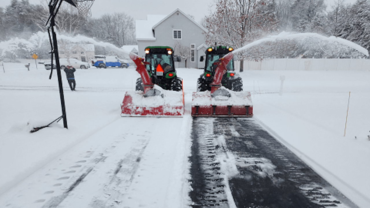 Two tractors with snow blowers clearing snow from a road during a snowstorm.