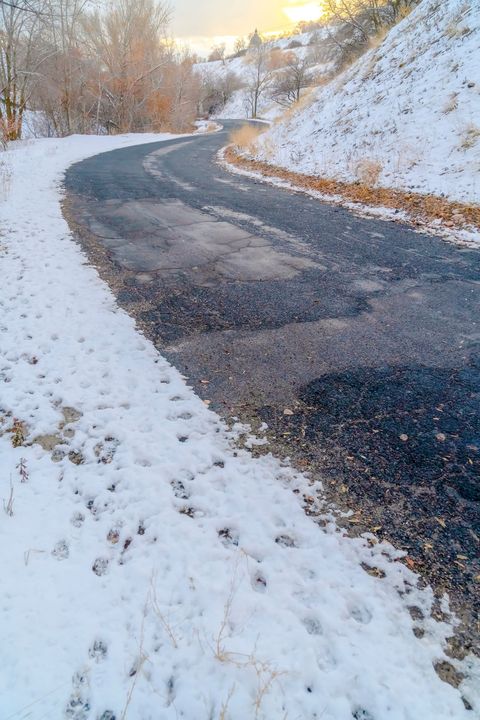 A winding asphalt road curves through a snowy landscape, featuring visible pavement patches and uneven surfaces.