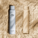 Silver aerosol can and a beige rectangular bar on a sandy background.