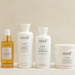Four KÉUNE hair care product bottles in white and amber on a light beige background