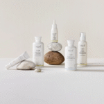 White cosmetic bottles and a tube arranged with stones on a light textured surface.