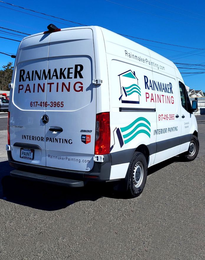 A white van with rainmaker painting written on the back is parked on the side of the road.