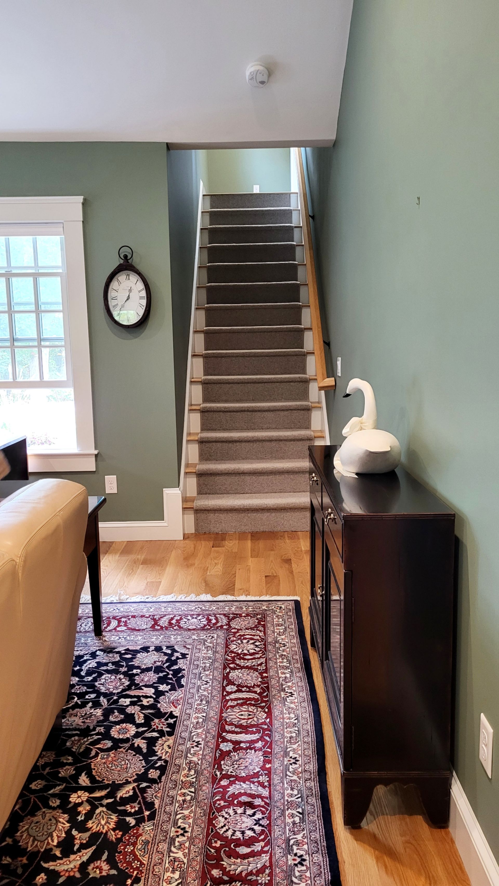 A living room with stairs leading up to the second floor and a clock on the wall.