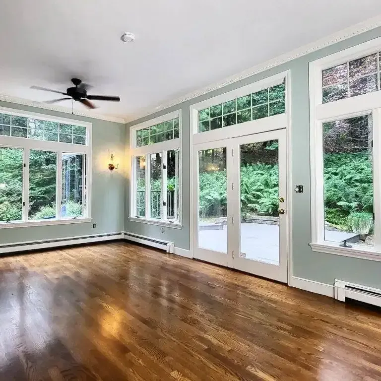 An empty living room with hardwood floors , a ceiling fan , and lots of windows.