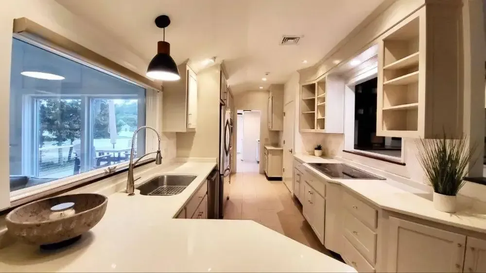 A kitchen with white cabinets , a sink , and a large window.