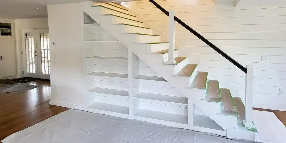A white staircase with shelves underneath it in a living room.