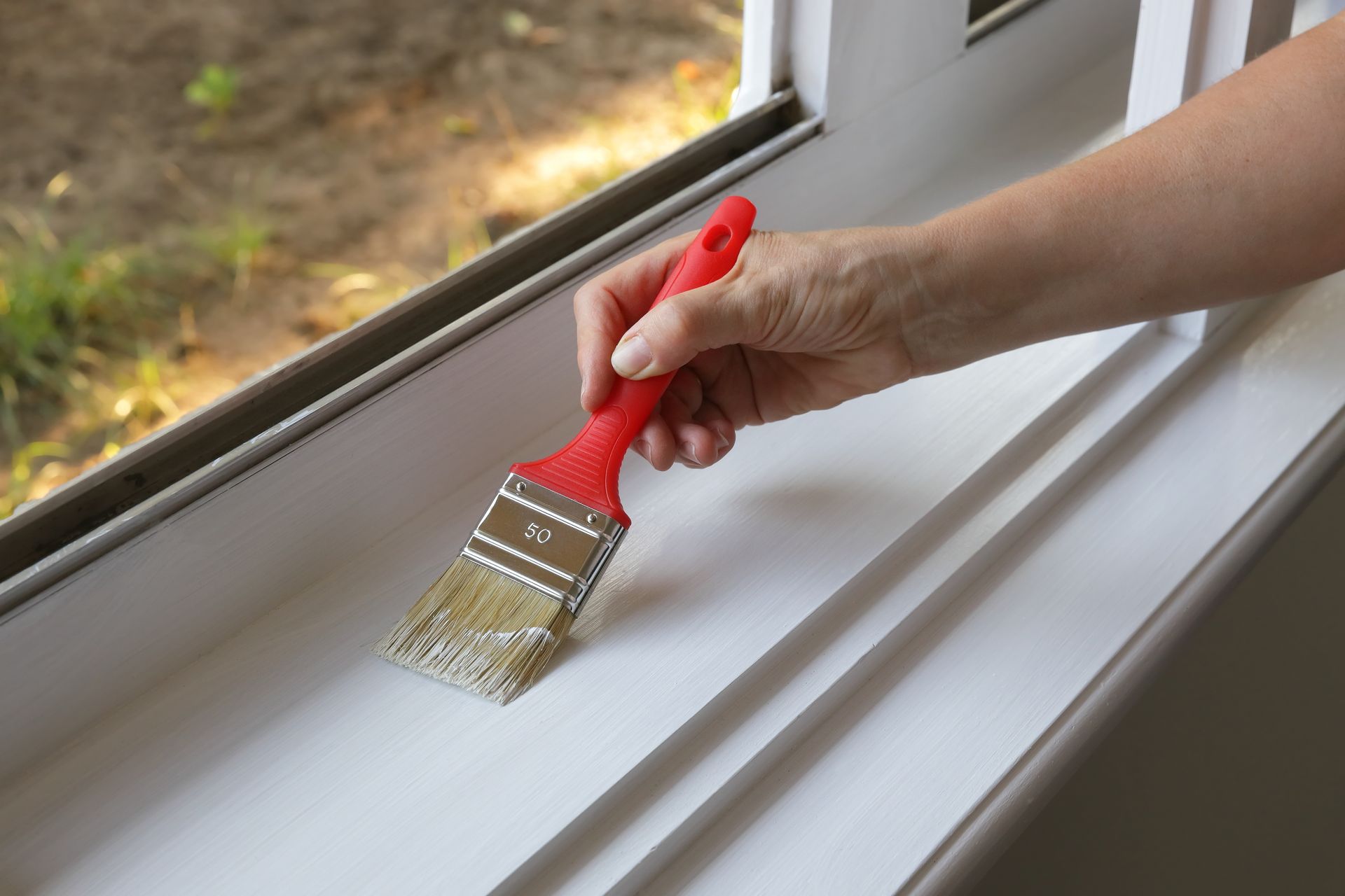 A person is painting a window sill with a brush.