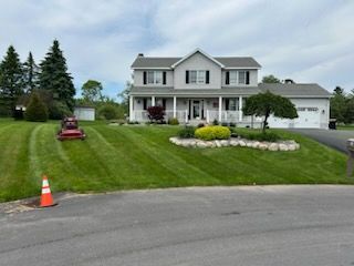 A large white house with a lawn mower in front of it.