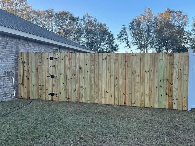 Wooden fence attached to a brick house. Green grass and trees in the background.
