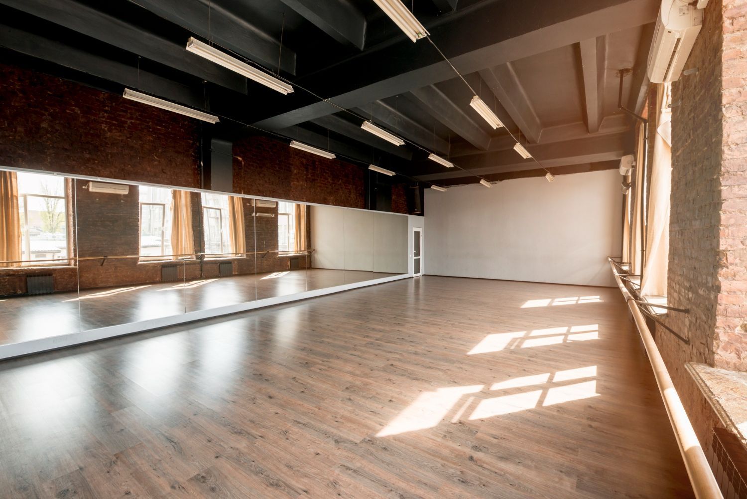 Empty dance studio with mirrors, brick walls, and hardwood floor.