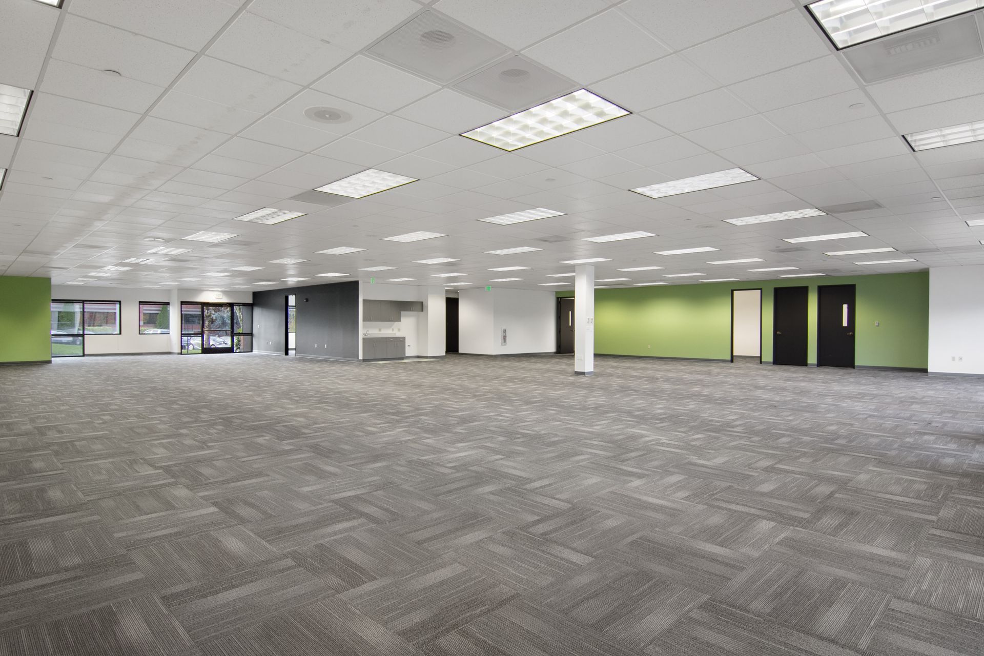 Empty office space with gray carpet, white ceiling, green and white walls, and black doors.