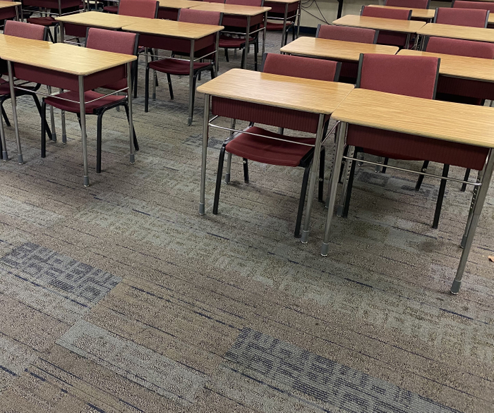 A row of wooden desks and chairs in a classroom.