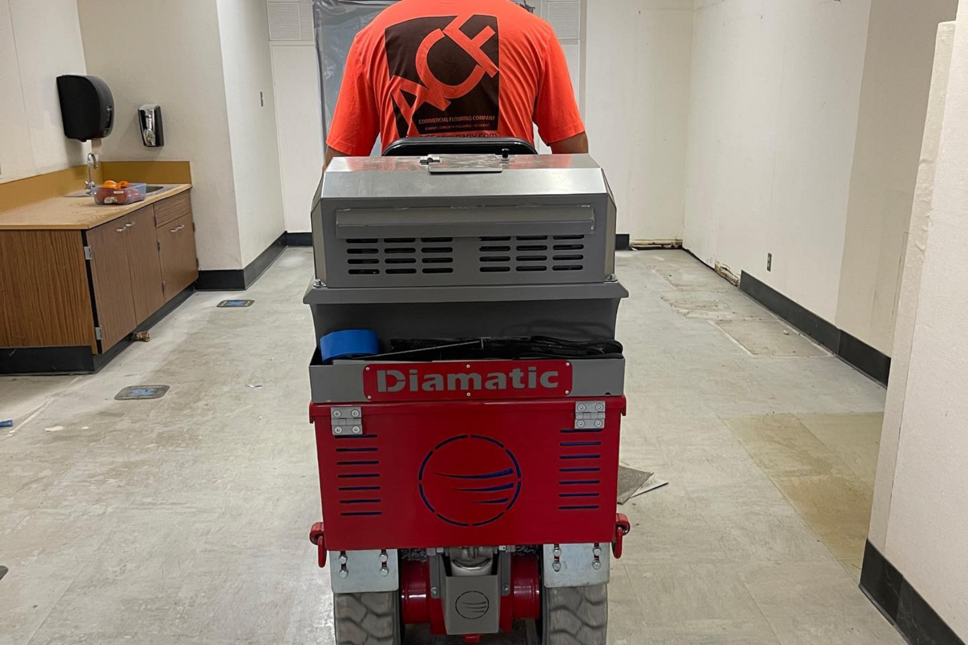 Person operating a red Diamatic floor cleaning machine in a hallway.